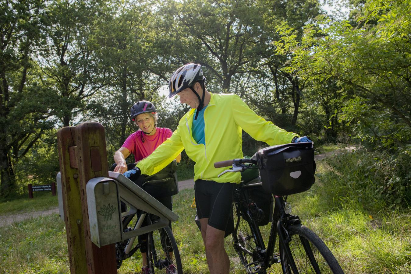 Ældre par på cykeltur kigger på skilt ved Gudenåens udspring