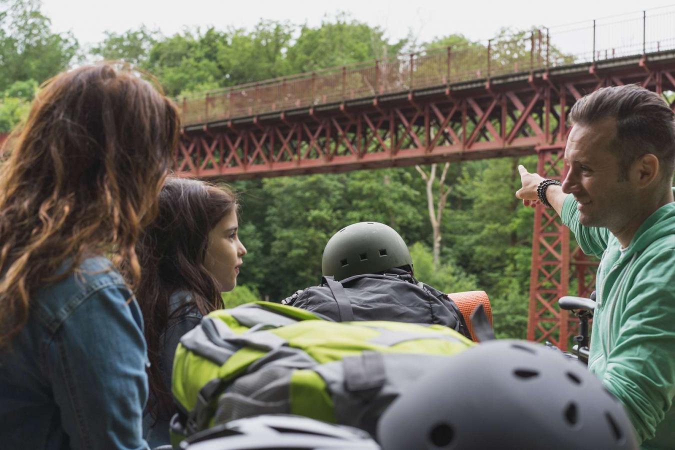Far peger på Den Genfunde Bro med datter og hustru ved bord-bænke-sæt i Bakkelandet