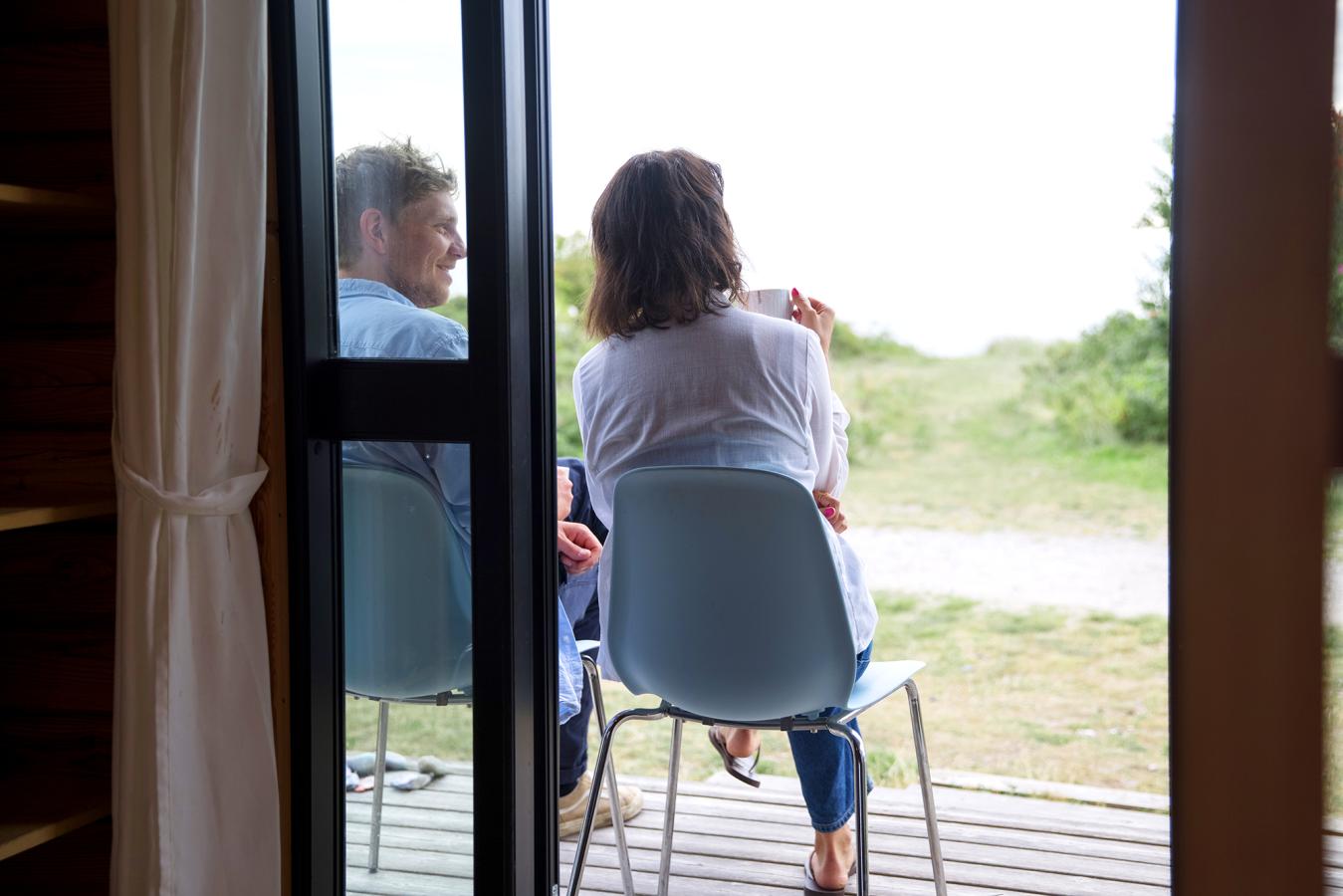 Par hygger sig på terrassen foran hytte på Tunø Teltplads i Destination Kystlandet
