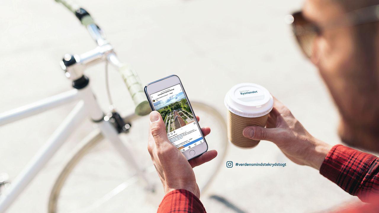 Mand kigger på mobil med Destination Kystlandet på skærmen og cykel og to-gokaffe