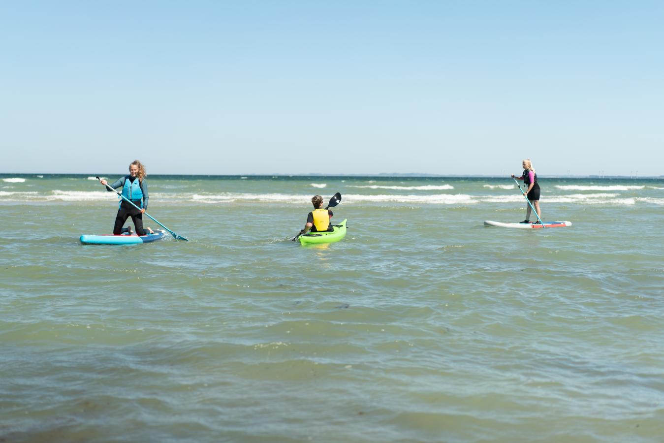 Frauen auf SUP-Boards und Mann im Meerkajak am Saksild Strand