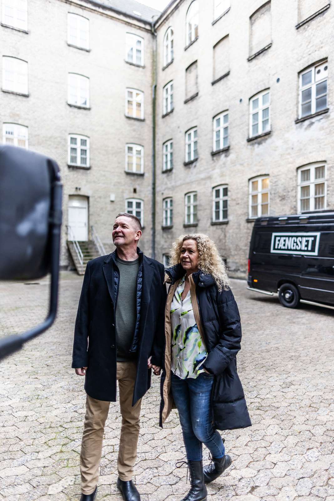 Mand og Kvinde kigger på en bil i en muret fængselsgård