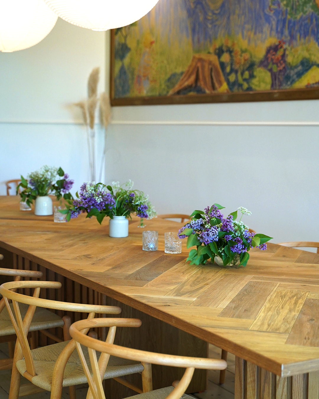 Bord i sildeparket med y-stole sat til og lilla syrener på bordet